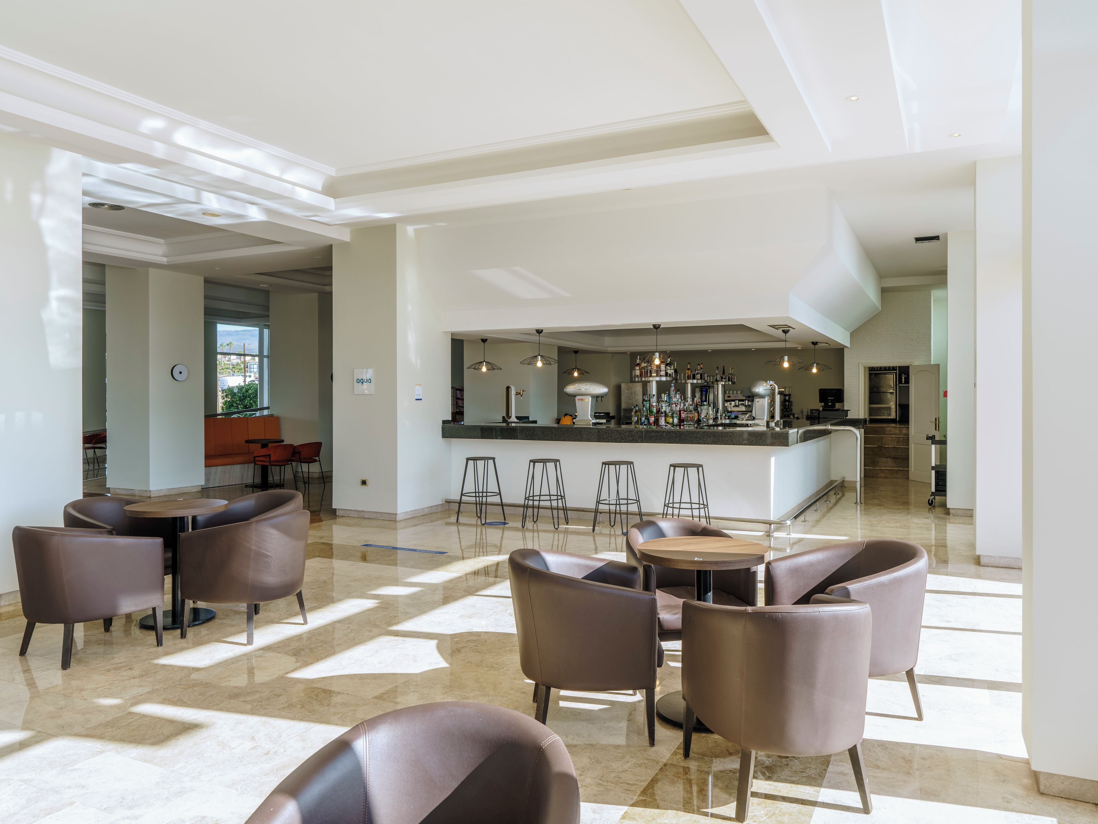 En moderne hotellobby med barområde, siddepladser og udsigt gennem en åben dør.