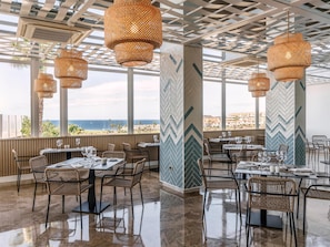 A restaurant with outdoor seating, wicker chairs, and hanging rattan lamps. Tables are set with wine glasses and plates. - Alua Atlantico Golf (San Miguel de Abona)