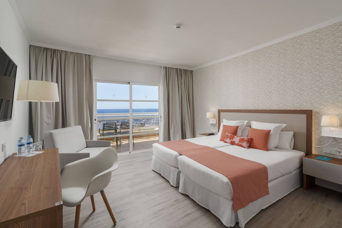 A hotel room with a bed, a desk, a chair, and a view of the city through the window.