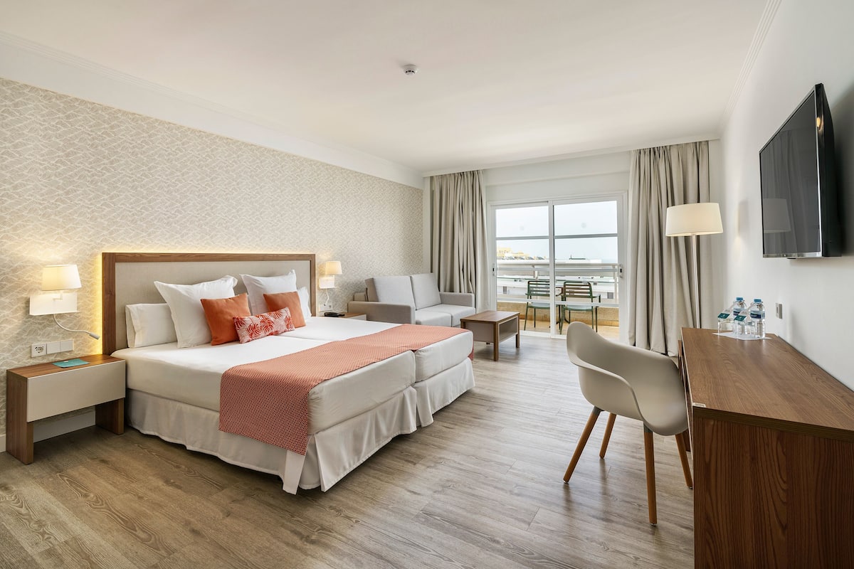 A hotel room with a bed, bedside tables, a desk, a chair, and a TV.
