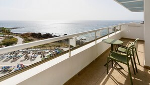 A balcony with a view of the ocean, a table, and two chairs. - Alua Atlantico Golf (San Miguel de Abona)