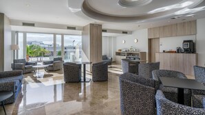 A modern hotel lobby with a spacious seating area, a kitchen, and large windows offering a view of the city. - Alua Atlantico Golf (San Miguel de Abona)