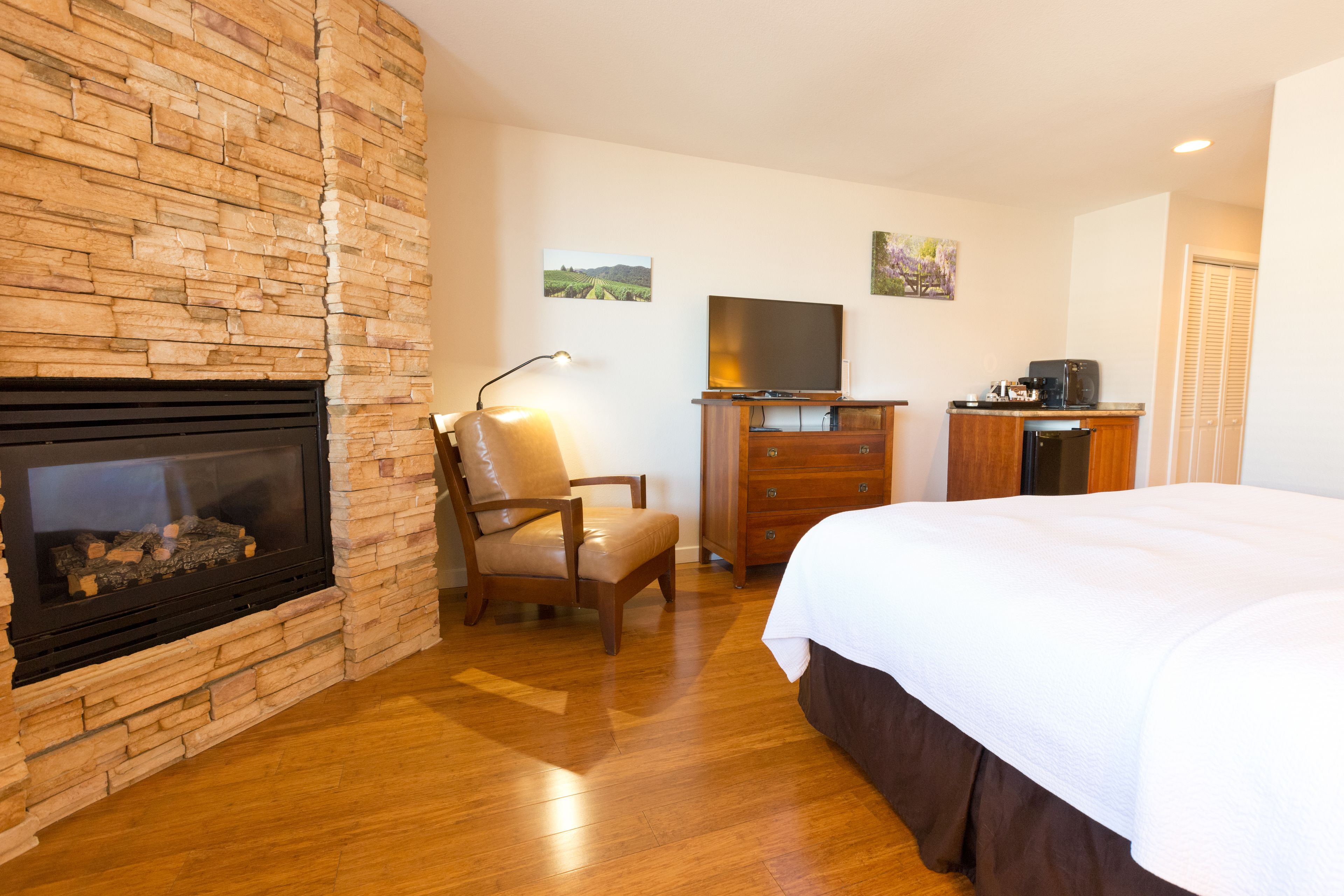 Habitación de hotel con chimenea de piedra, un televisor de pantalla plana, cómoda de madera y cama con ropa blanca.
