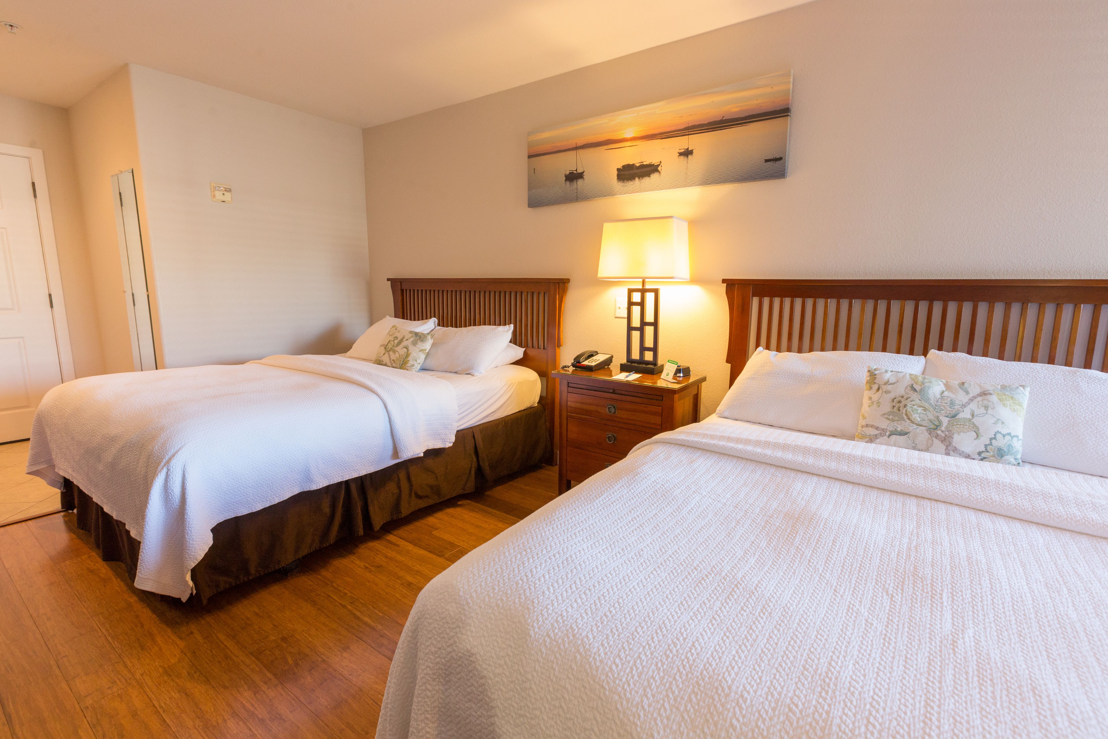 A hotel room with two beds, a bedside table with a lamp, and a painting on the wall.