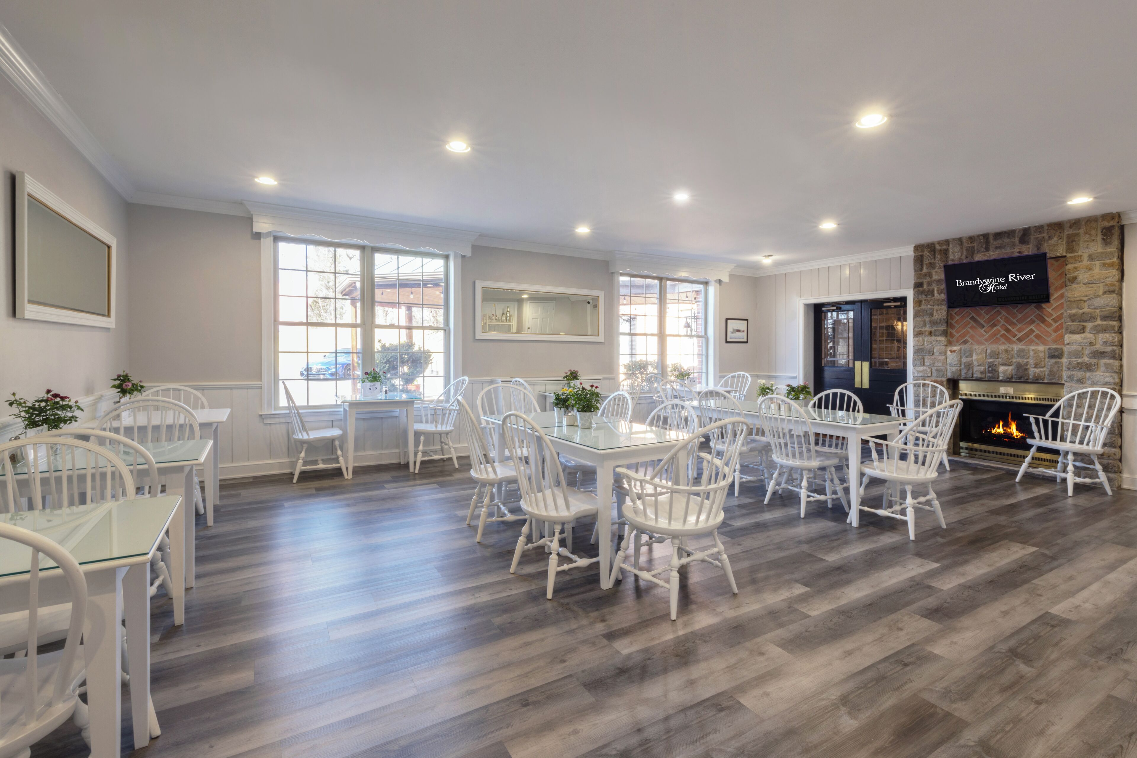 A dining area with white chairs and tables, a fireplace, and large windows.
