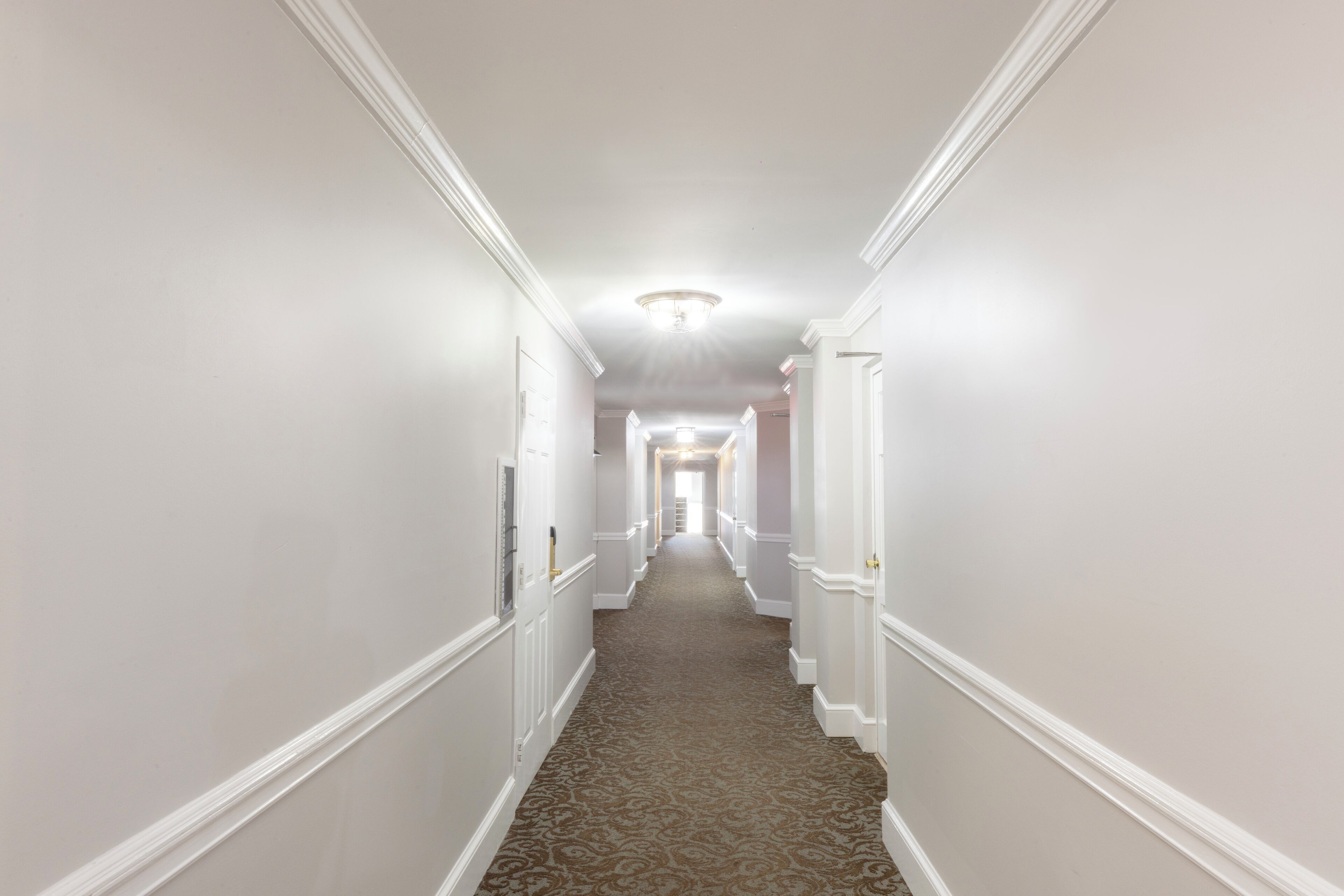 Un long couloir étroit aux murs blancs et au tapis à motifs.