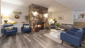 Un salón con chimenea de piedra, sillones azules, una mesa de centro blanca y una repisa de chimenea con adornos.