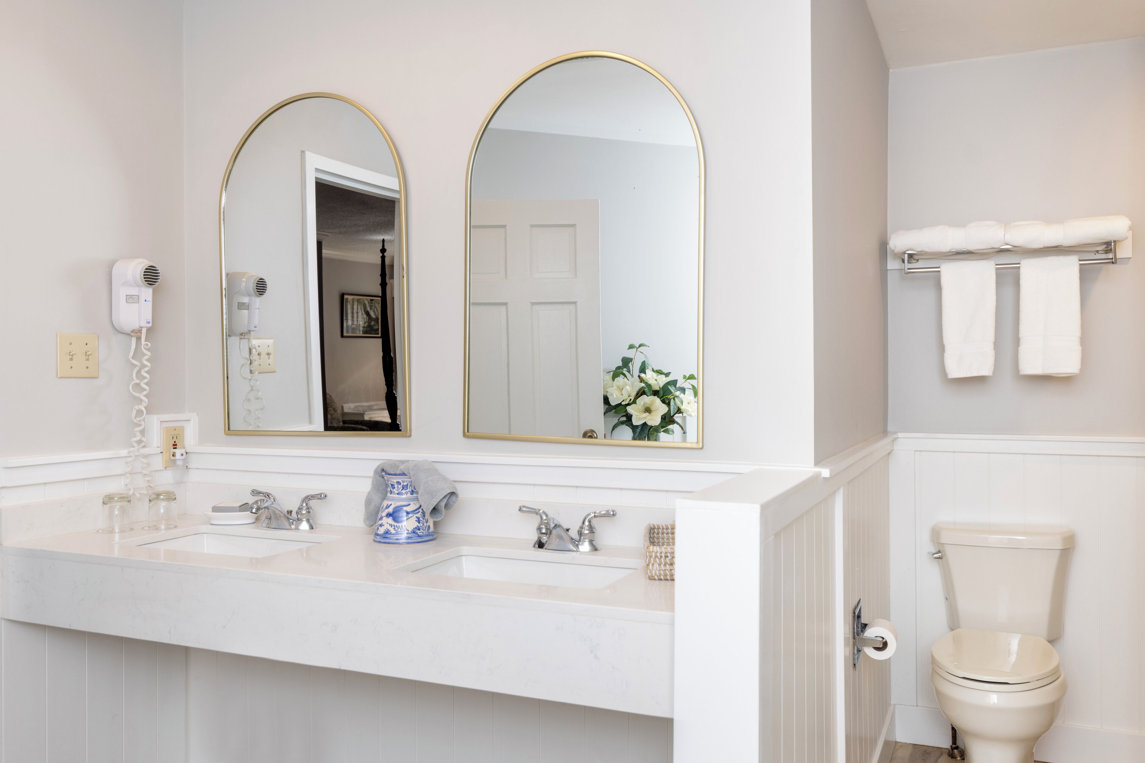 A bathroom with a white sink, two mirrors with gold frames, a white toilet, and a towel rack with towels.