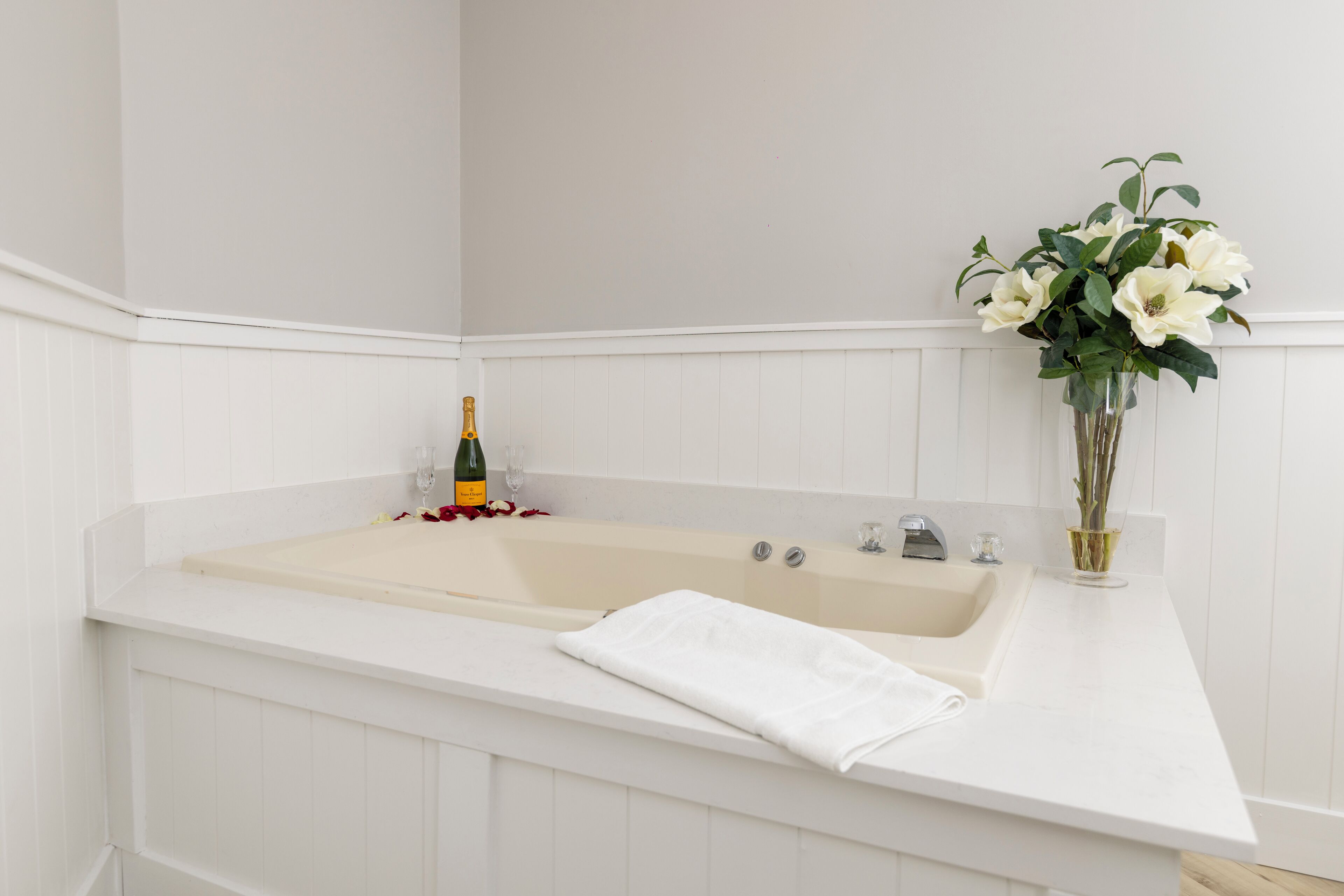Ein Badezimmer mit einer Badewanne, einer Champagnerflasche und einem Blumenstrauß.