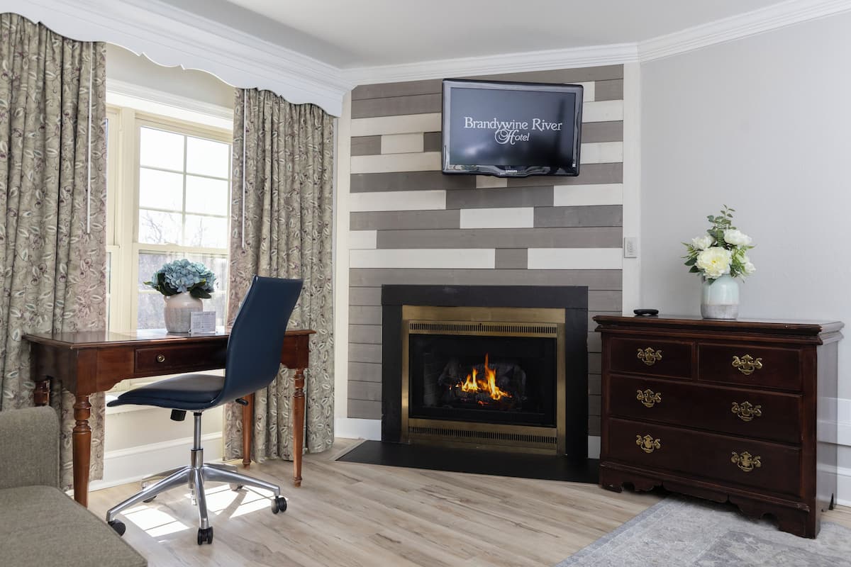 A room with a fireplace, a television mounted above it, a desk with a chair, and a dresser with drawers.