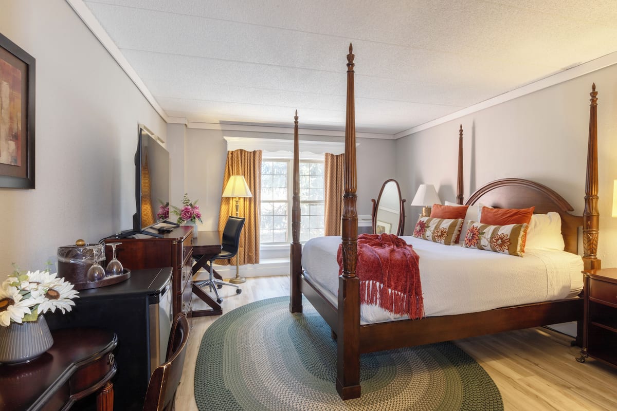 A four-poster bed with a wooden frame, a desk with a lamp, and a chair.