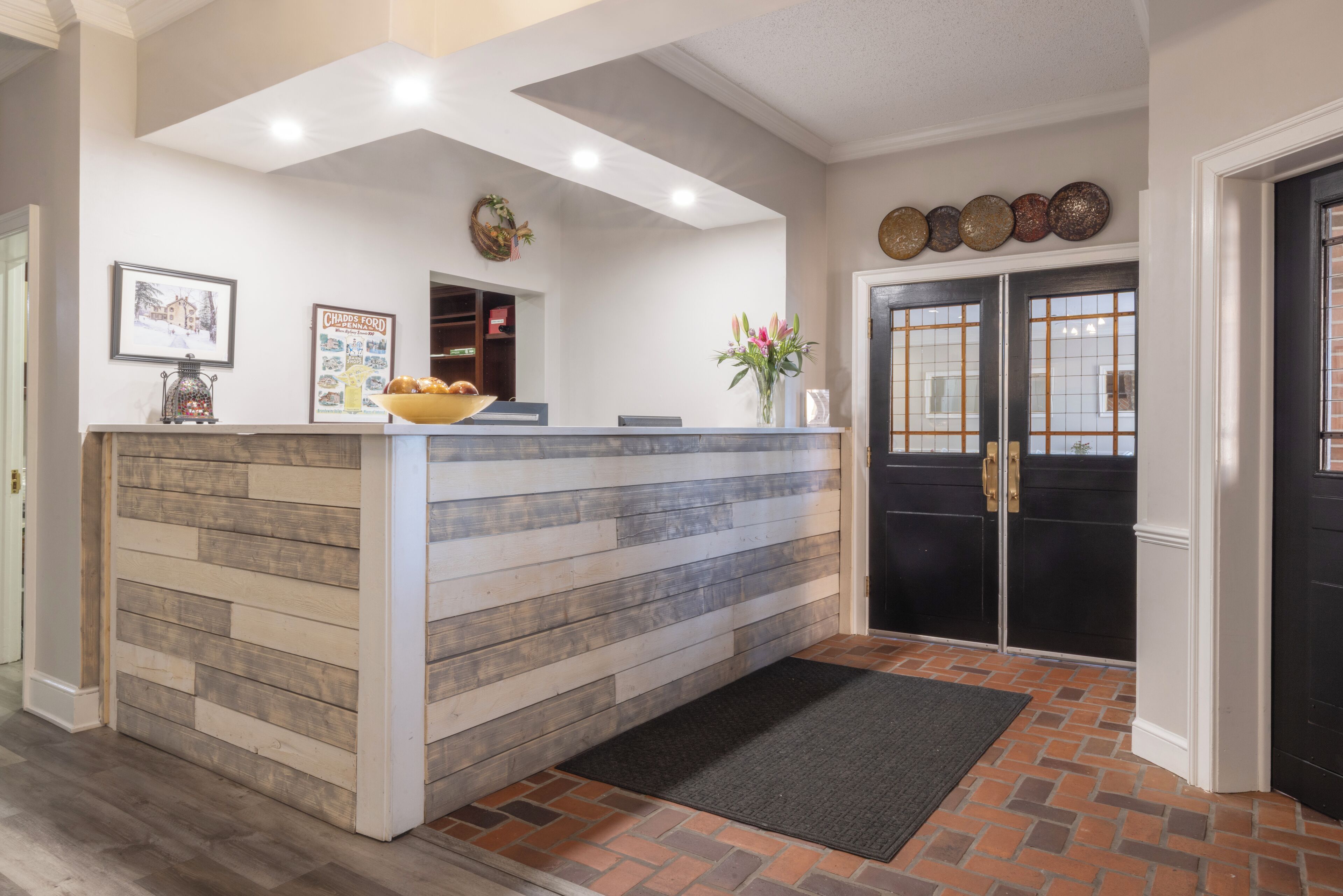 A reception area with a wooden reception desk, a black door with glass panels, and a black mat at the entrance.