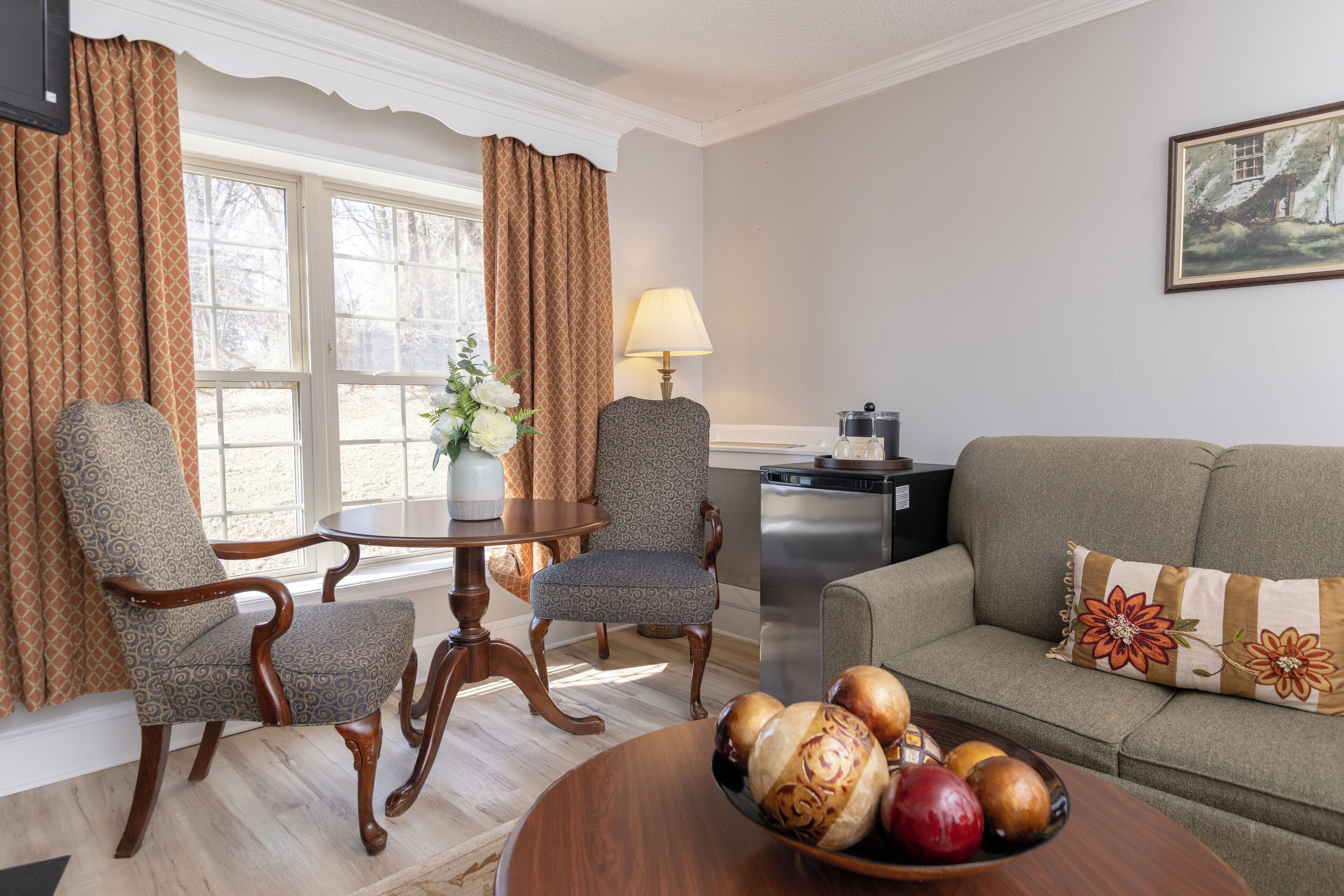 Una sala de estar con un sofá, dos sillones, una mesa de centro con un frutero, una lámpara y un cuadro en la pared.