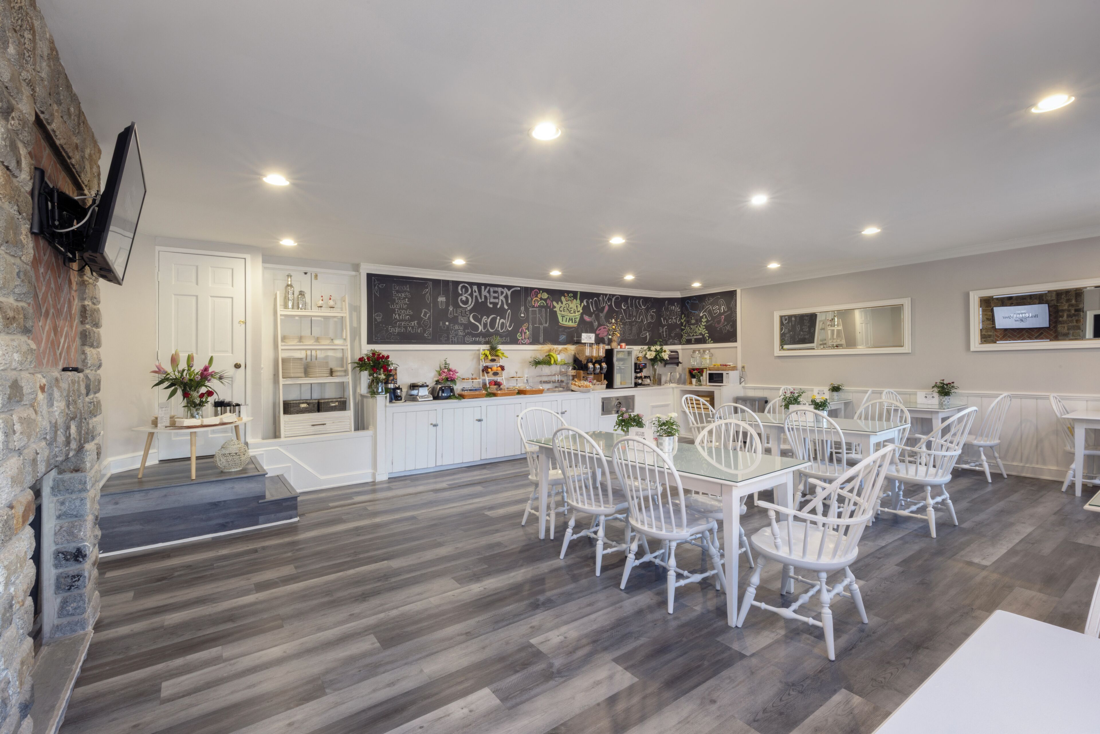 A spacious kitchen with white cabinetry, a chalkboard wall, and a dining area with white chairs and a large table.