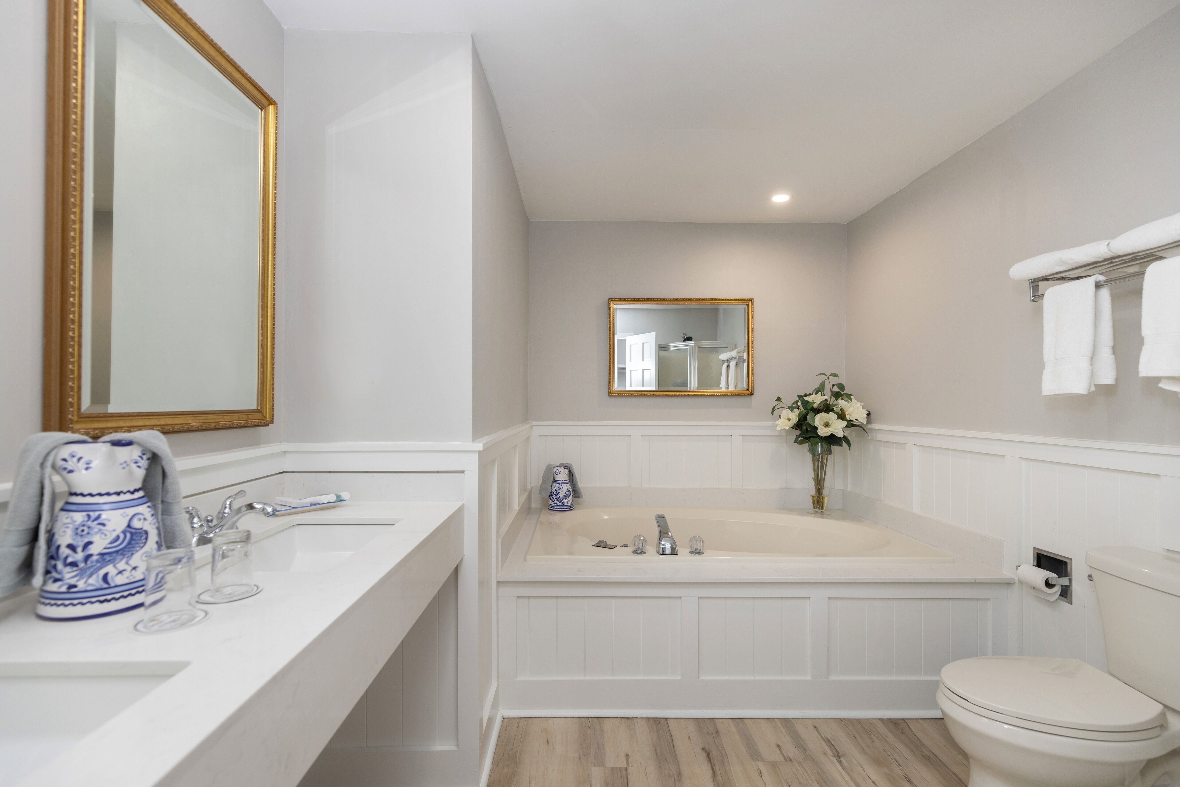 A bathroom with a white vanity, a bathtub, a toilet, and a mirror with a gold frame.