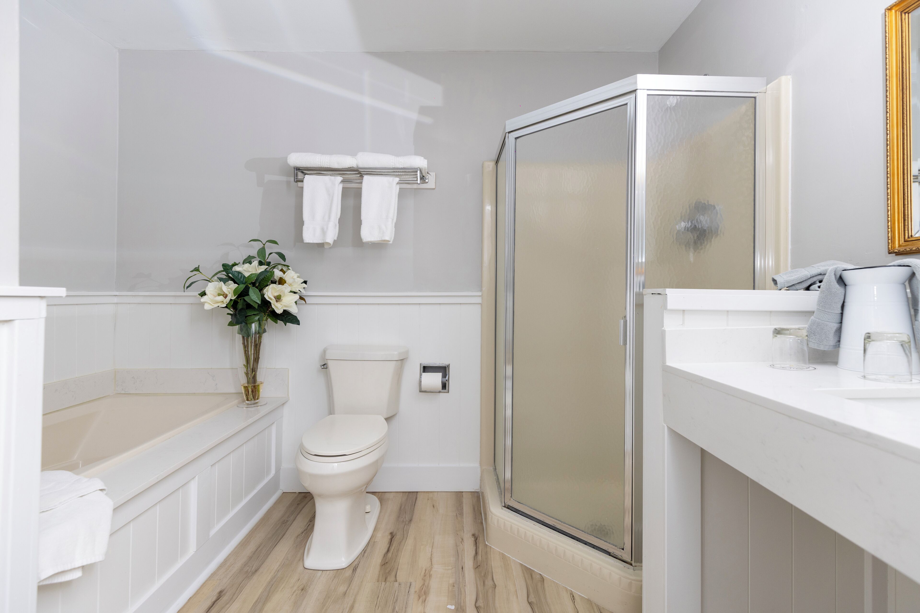 A modern bathroom with a toilet, a glass shower enclosure, a sink with a mirror, and a vase with flowers.