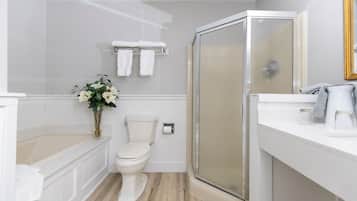 A modern bathroom with a toilet, a glass shower enclosure, a sink with a mirror, and a vase with flowers.