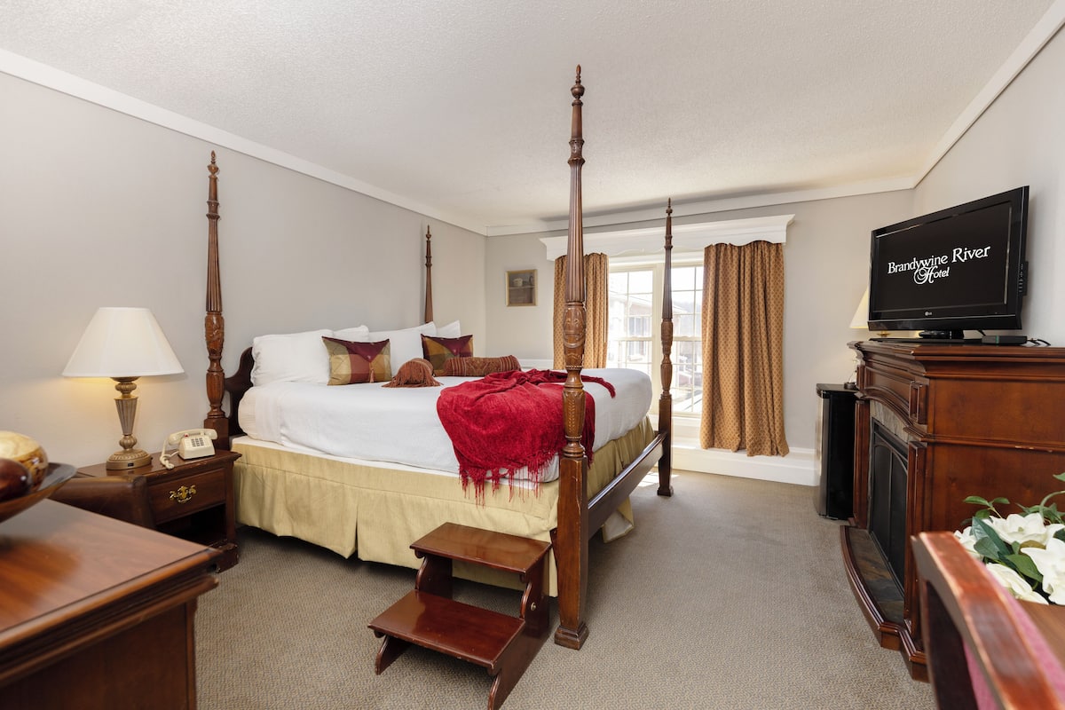 A four-poster bed with a red throw blanket, a television, and a wooden nightstand with a lamp.