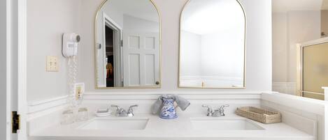 A bathroom with two sinks, a hairdryer, and a vase.