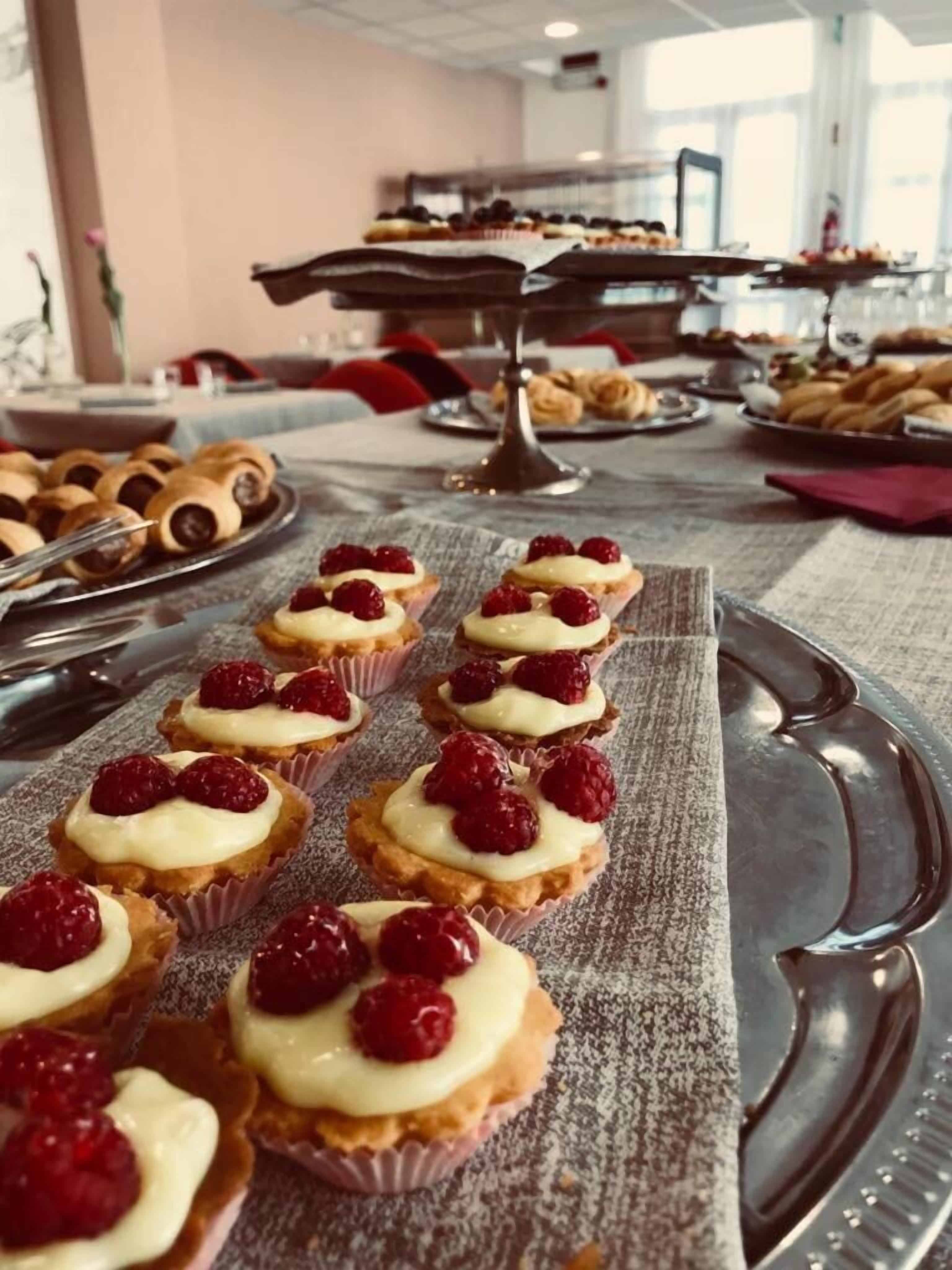 A buffet table with various pastries and desserts, including raspberry-topped tarts and chocolate rolls.
