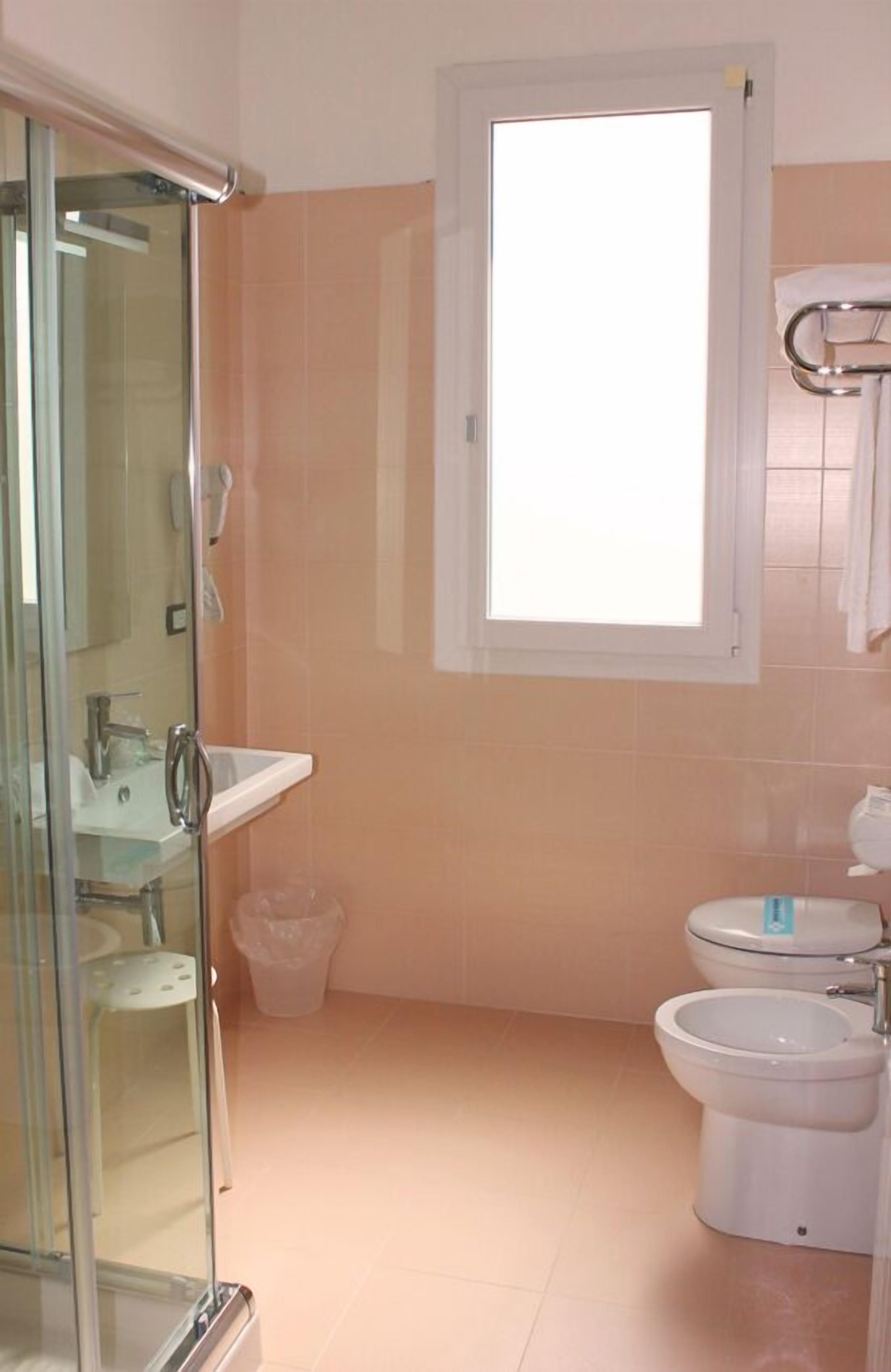 A bathroom with a glass shower enclosure, a sink, a toilet, and a bidet.