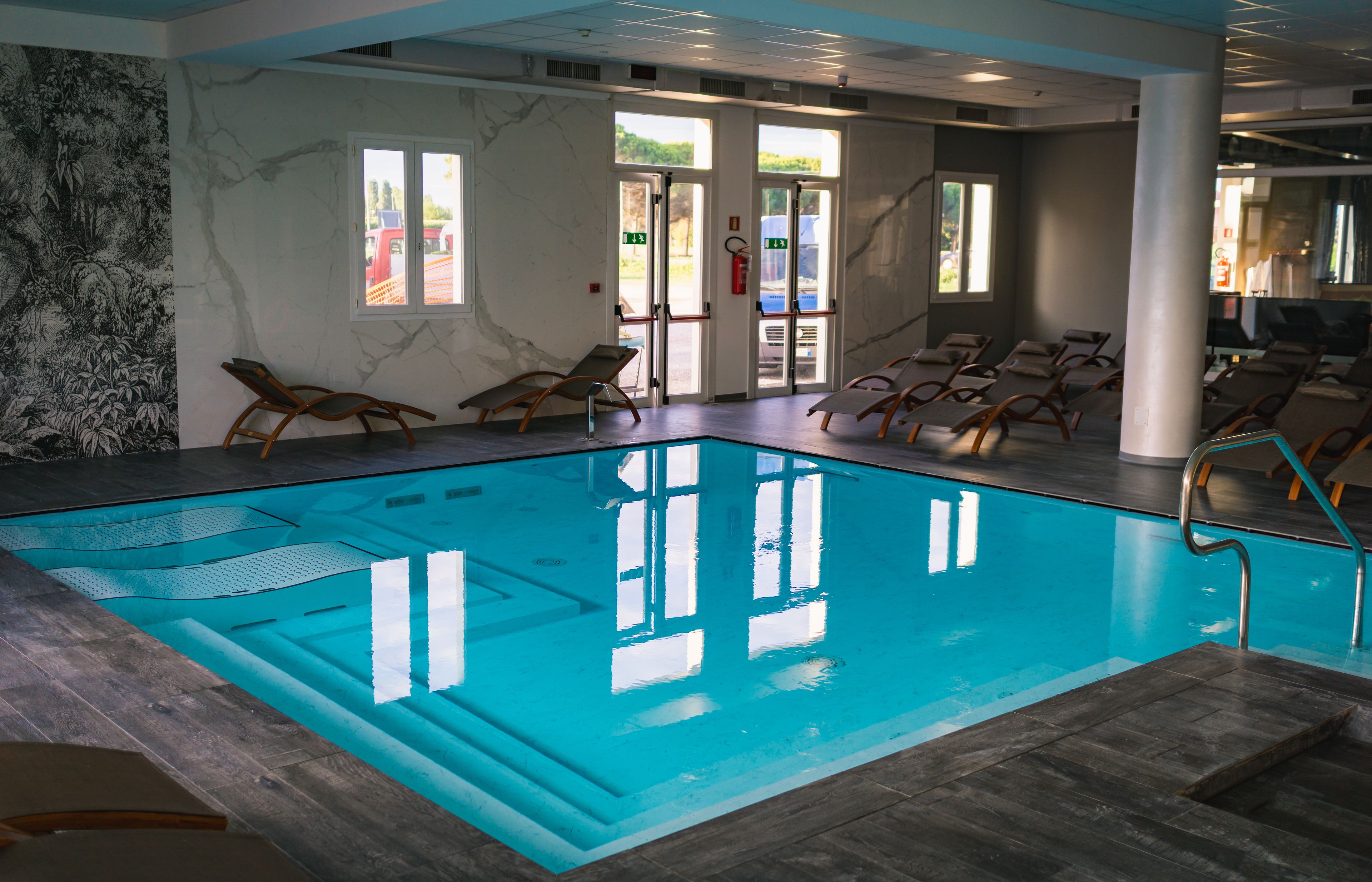 An indoor swimming pool with clear water, wooden loungers, and a mural on the wall.