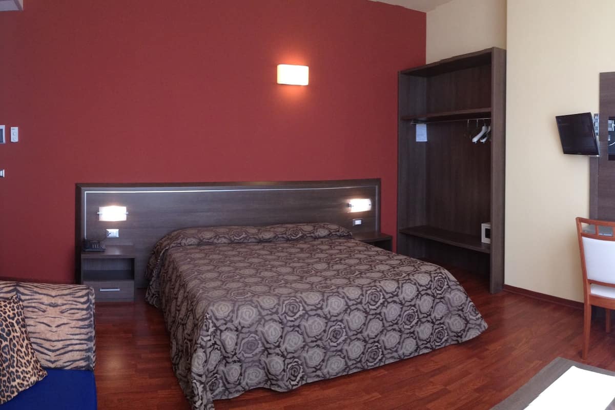 A bedroom with a bed, a desk, a chair, a TV, and a wardrobe.