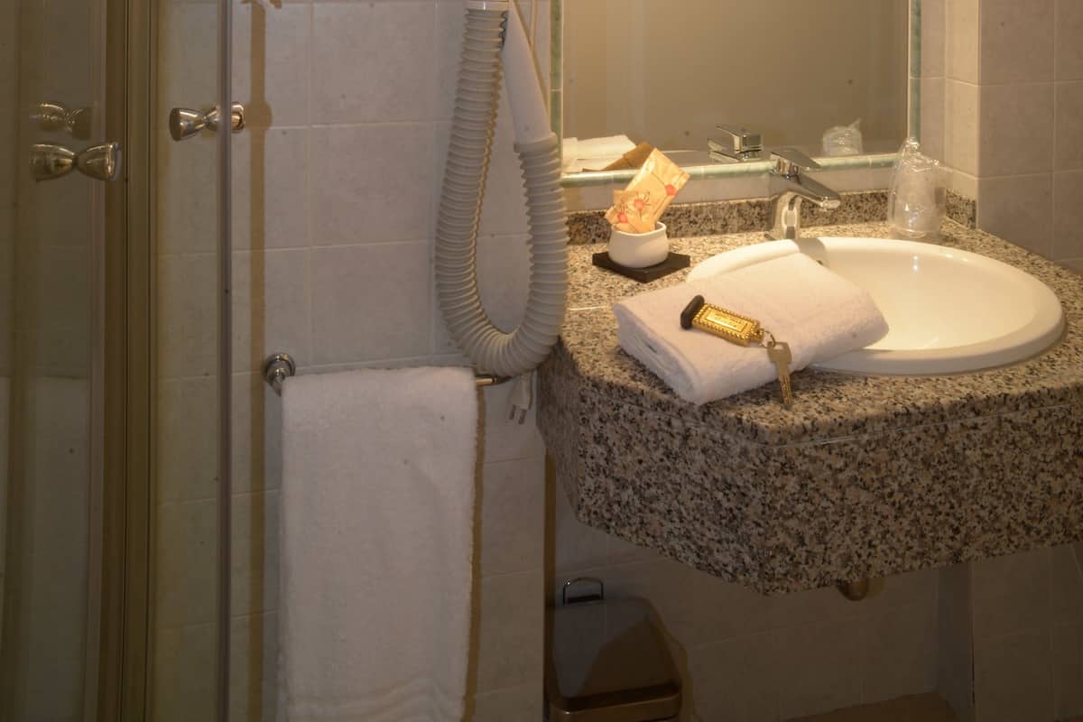 A bathroom with a glass shower door, a white towel hanging on the door, a hairdryer, and a sink with a mirror above it.