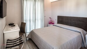 Habitación de hotel con cama, un escritorio con silla, televisor montado en la pared y ventana con cortinas.