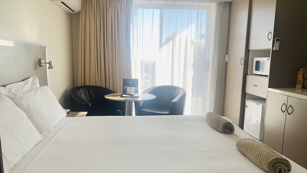 A hotel room with a bed, a desk, a chair, a small table, a microwave, and a cabinet. - Adina Place Motel Apartments (Launceston)