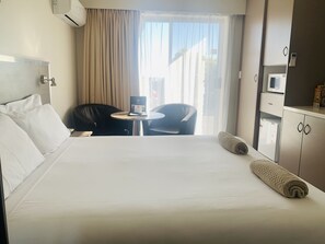 Quarto de hotel com cama, escrivaninha, cadeira, mesa pequena, micro-ondas e armário.