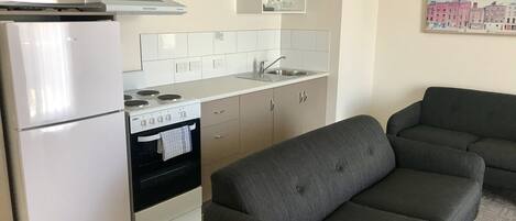 A compact kitchen with a microwave, stove, oven, and a grey sofa.