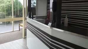 A modern reception desk with a computer, a telephone, and a window with blinds. - Adina Place Motel Apartments (Launceston)