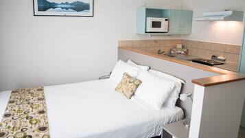 A neatly made bed with a patterned blanket, a bedside table with a lamp, and a microwave above a light blue cabinet.