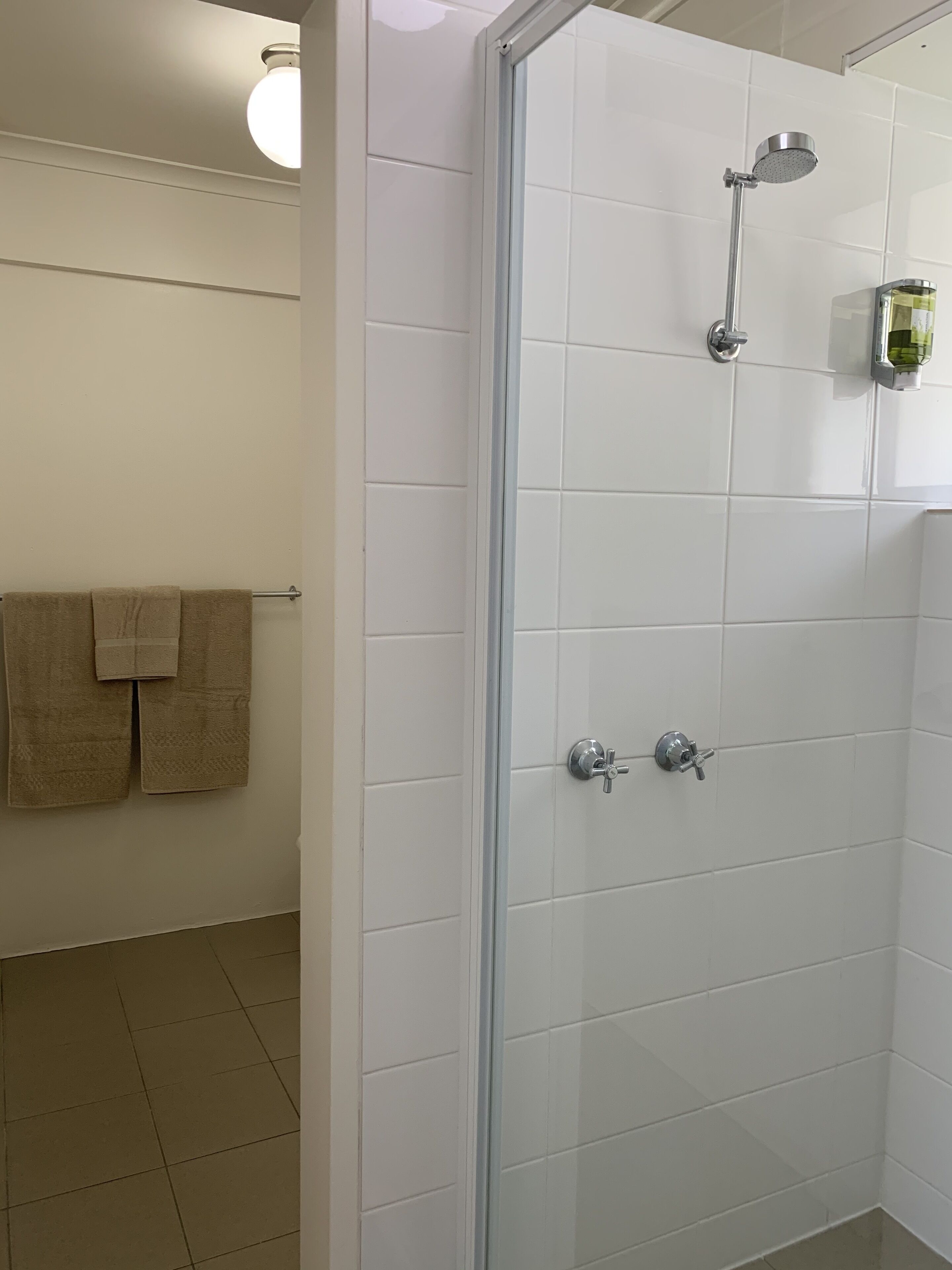 Un espace douche doté d’une porte en verre, de murs recouverts de carreaux blancs et d’un porte-serviettes avec deux serviettes.