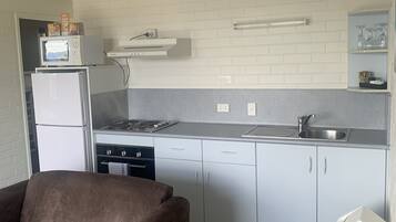 A compact kitchen with white cabinets, a microwave, and a stove. There is a brown sofa in the living area.