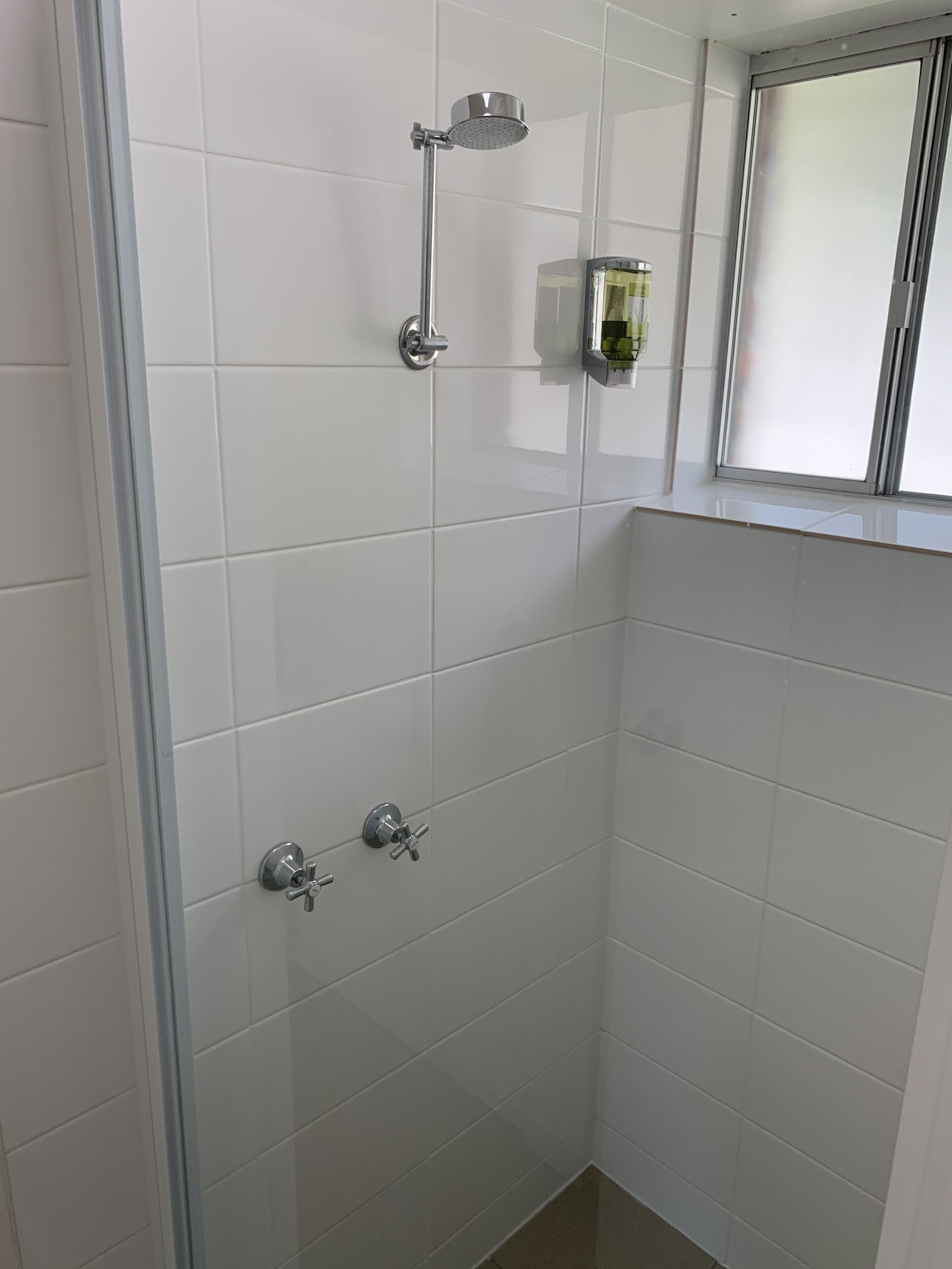 Un espacio de ducha pequeño y cerrado con puerta de cristal, ducha de mano y grifo empotrado.