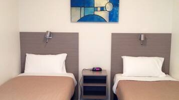 A hotel room with two beds, a small bedside table with a clock, and a wall art piece above the beds.