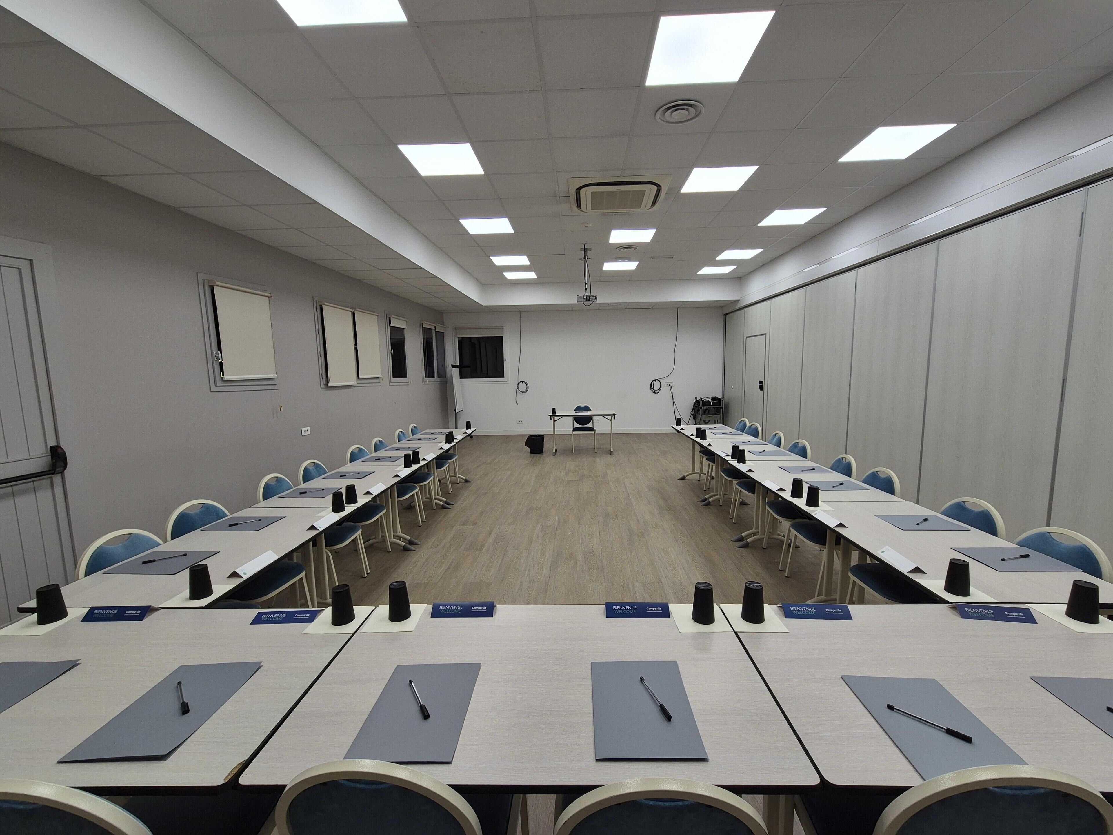 Une salle de conférence avec de longues tables, des plaques nominatives et des chaises.