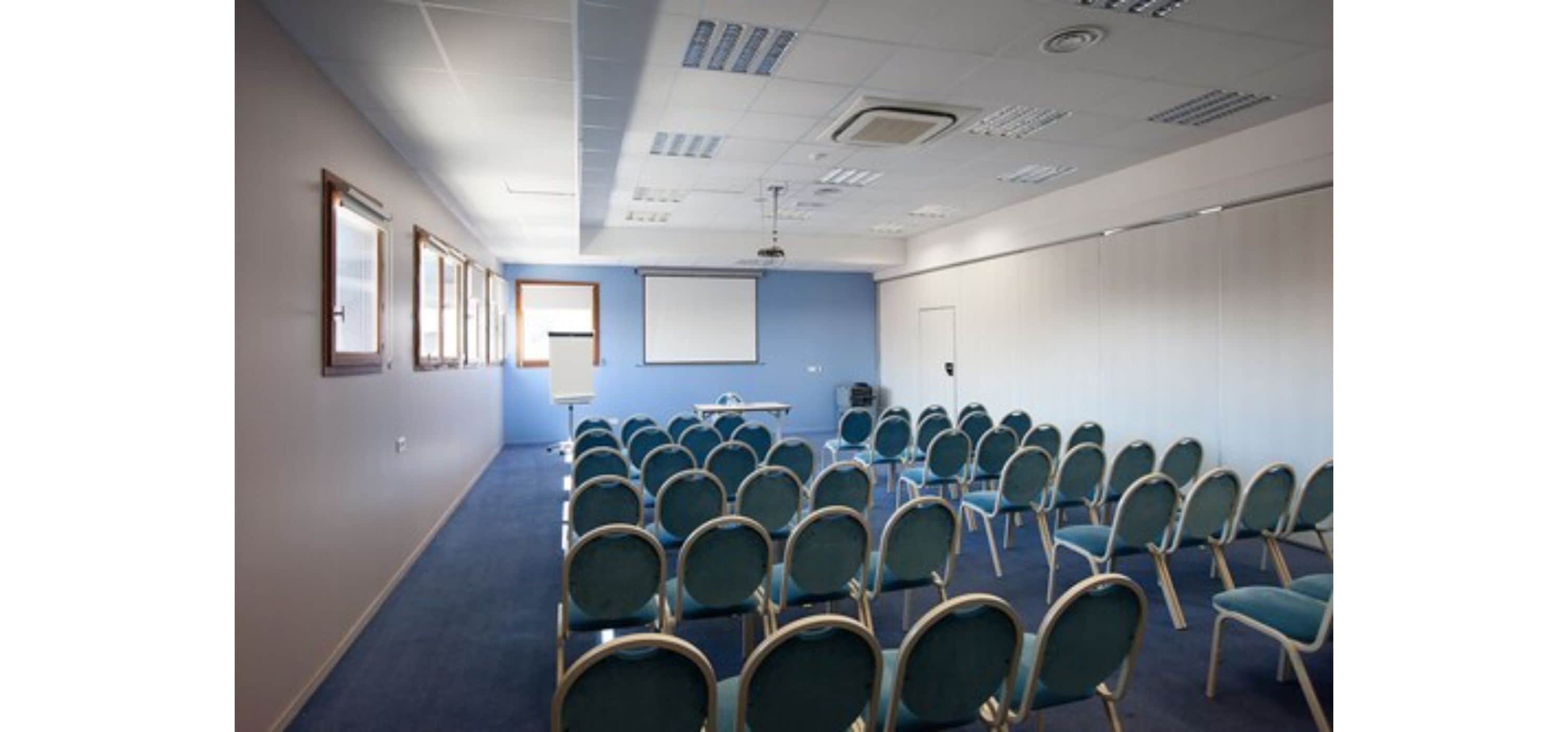 A conference room with rows of chairs, a projector screen, and a whiteboard.