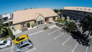 Un hôtel avec un toit recouvert de tuiles, un parking avec des places délimitées et un bâtiment sur lequel on peut lire l’inscription « Campanile ».
