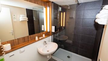 Un baño moderno con tocador de madera, lavamanos blanco, cabina de ducha con paredes de vidrio y un perchero para toallas.