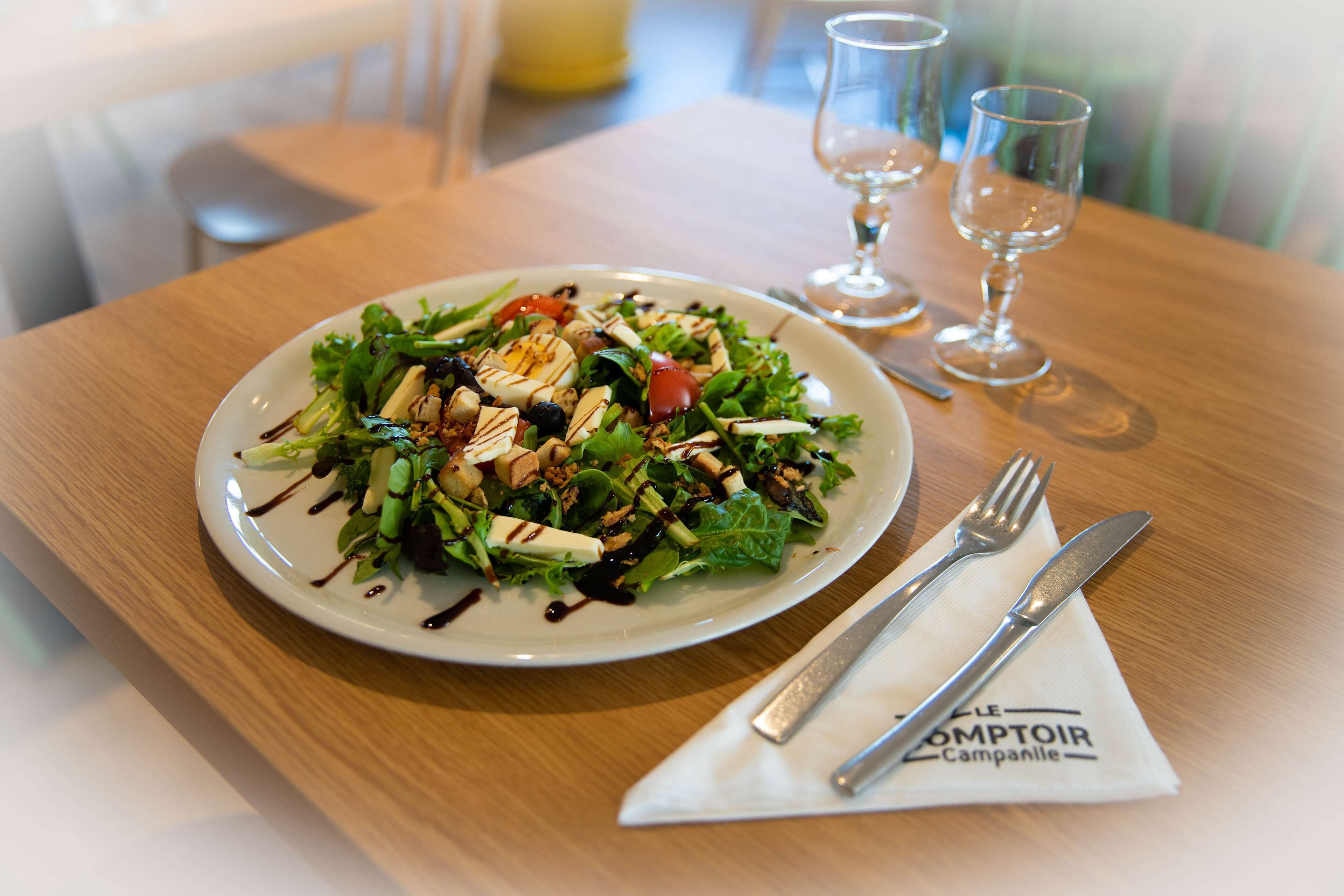 Une assiette de salade sur une table en bois, avec une serviette et des couverts.