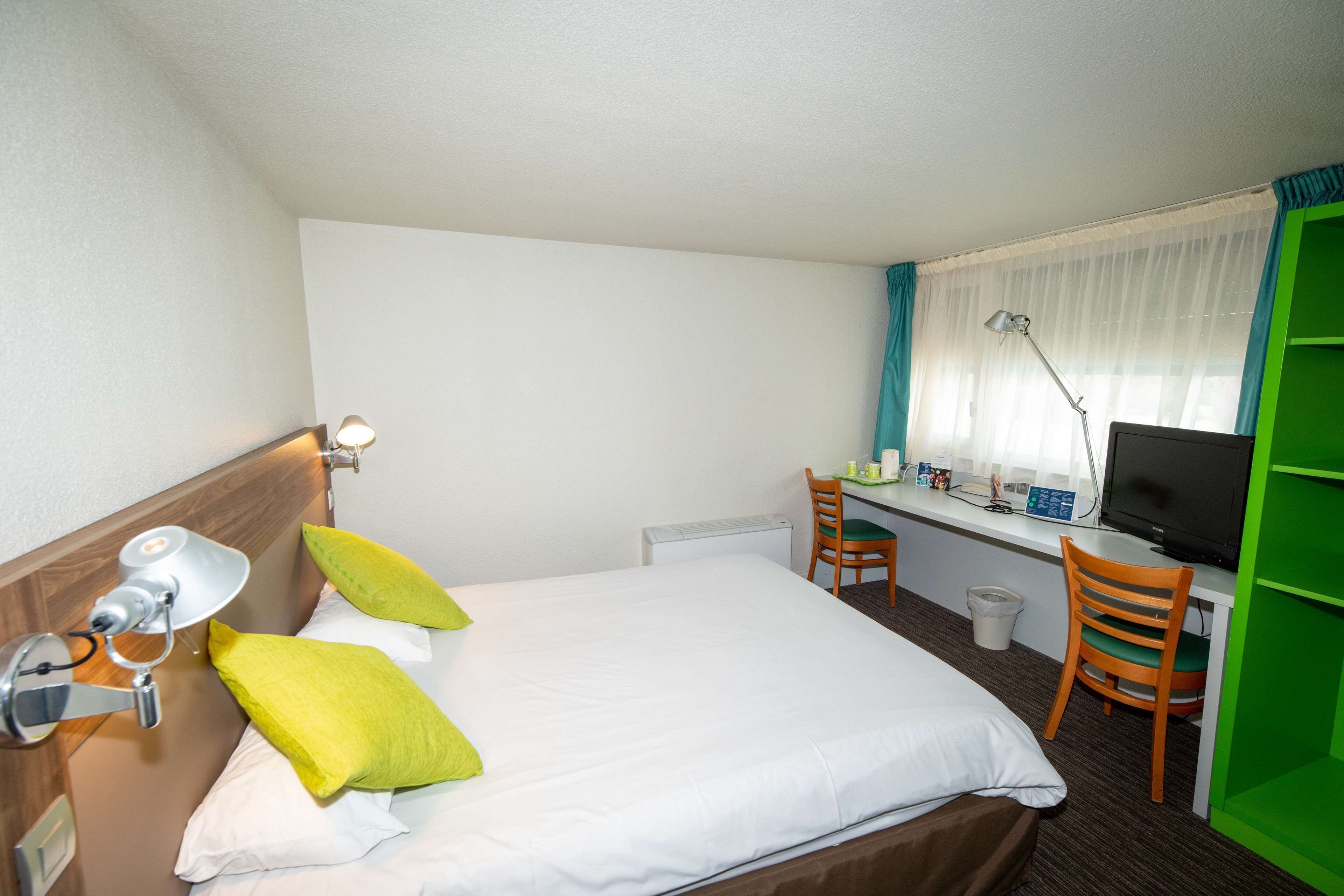 A hotel room with a bed, a desk with a computer, a chair, and a TV.
