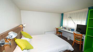 A hotel room with a bed, a desk with a computer, a chair, and a TV.