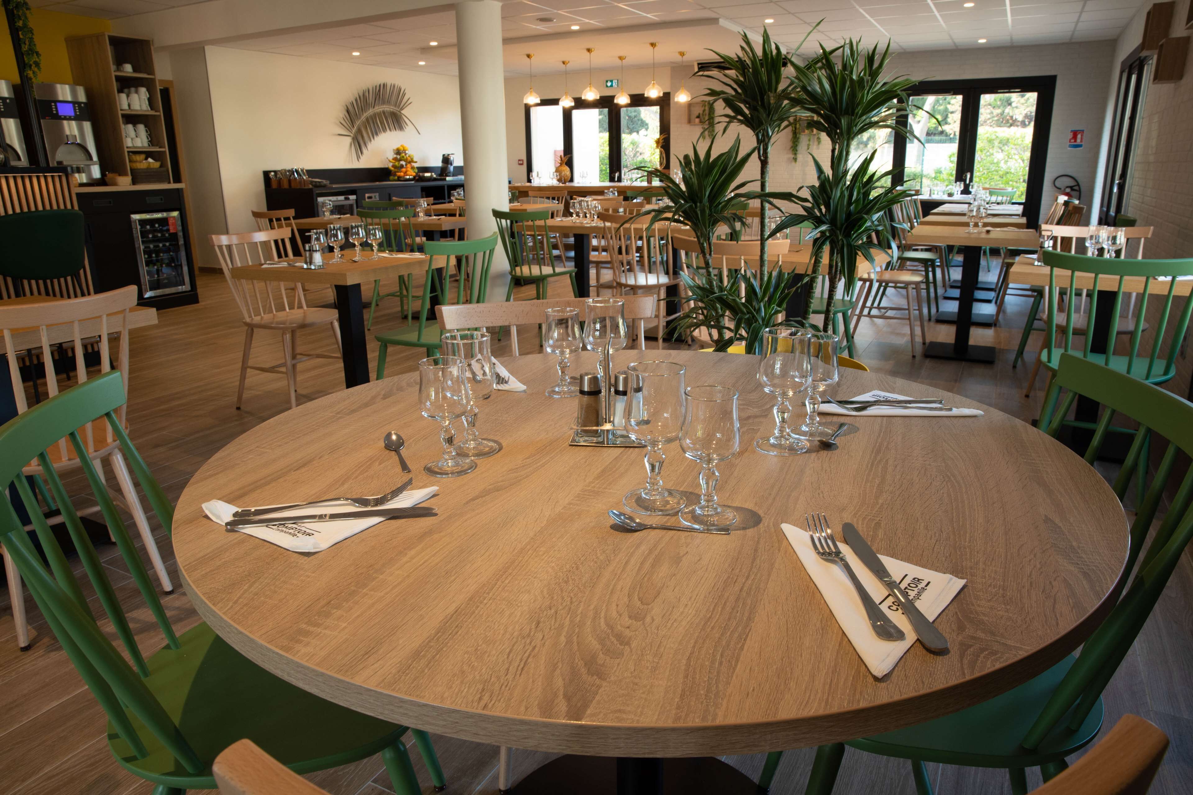 Un restaurant avec des tables rondes en bois, disposées pour le service, et entourées de chaises vertes.