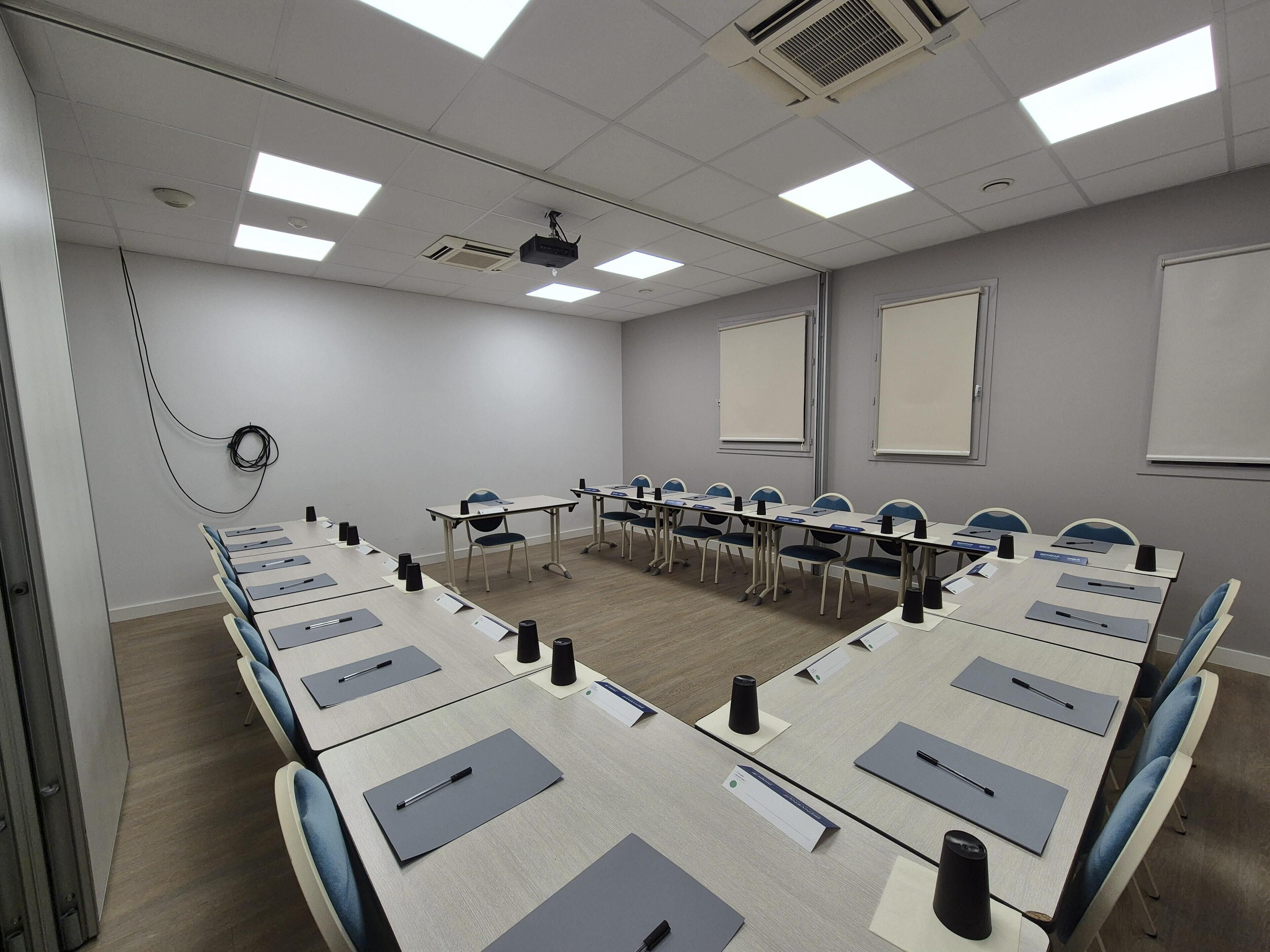 Uma sala de conferências com uma mesa comprida, cadeiras, porta-nomes e um projetor.