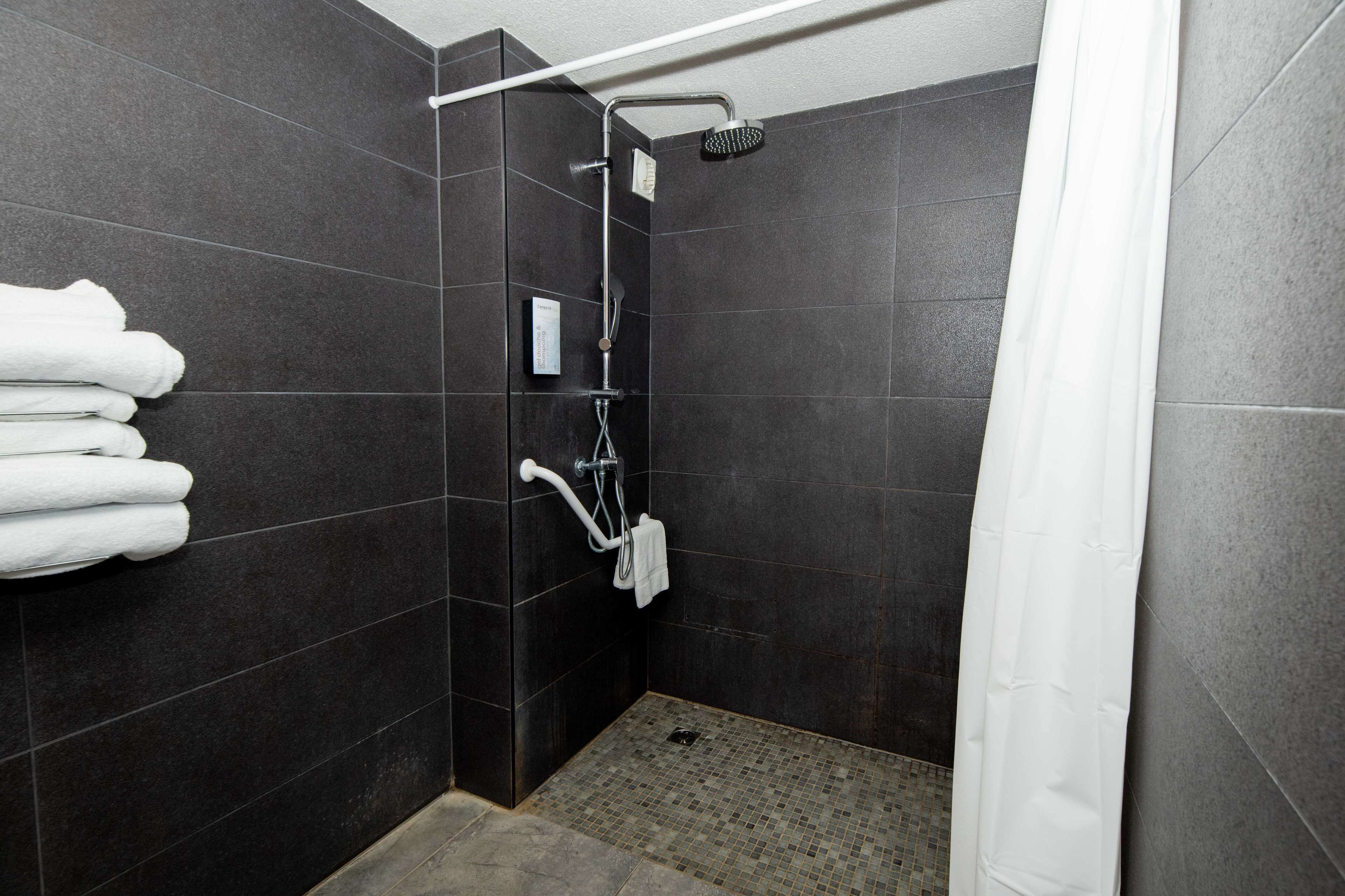 A modern shower area with dark tiles, a handheld showerhead, and a towel rack with folded towels.