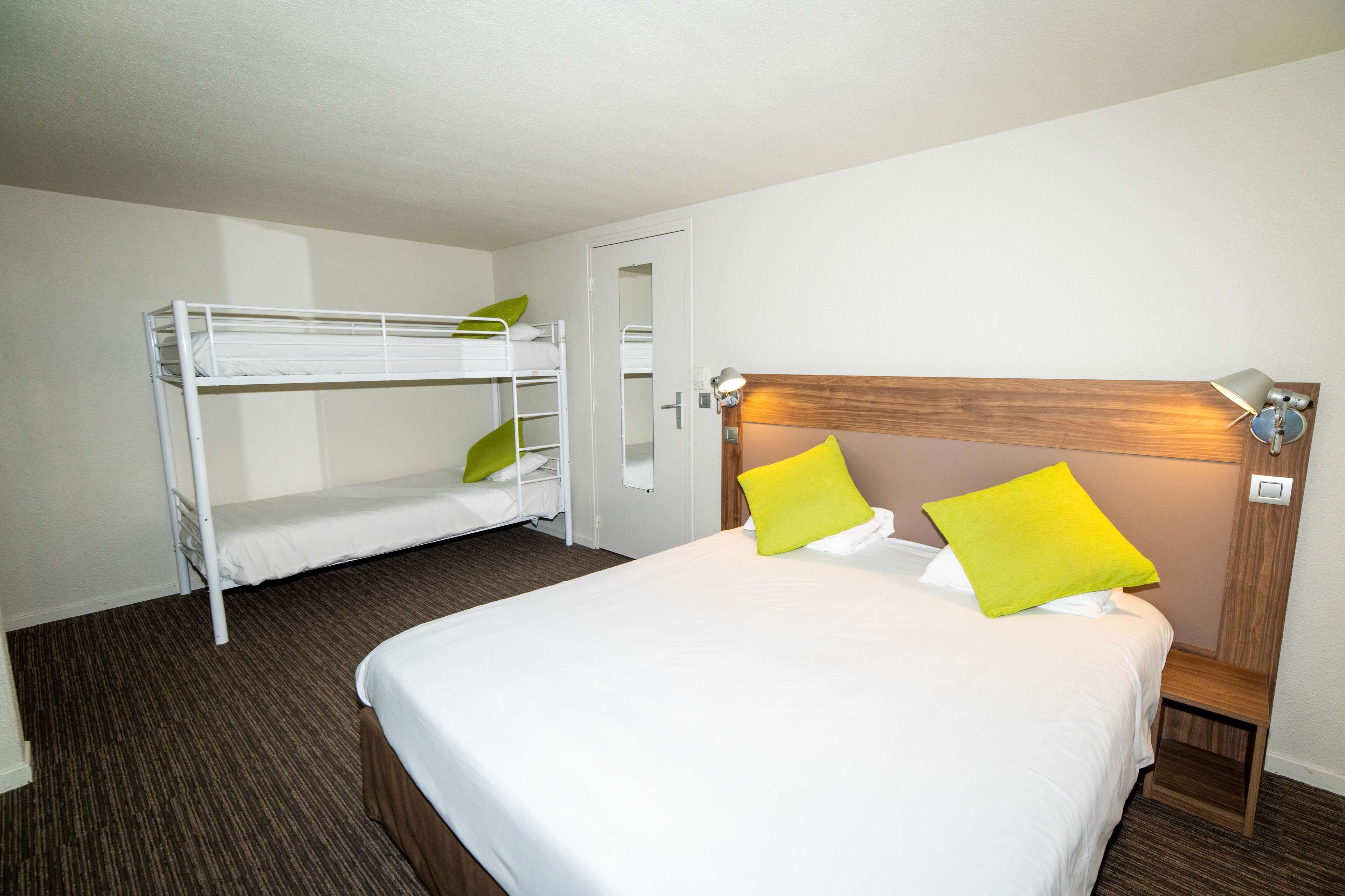 A hotel room with a single bed, a bunk bed, and a nightstand with a lamp.