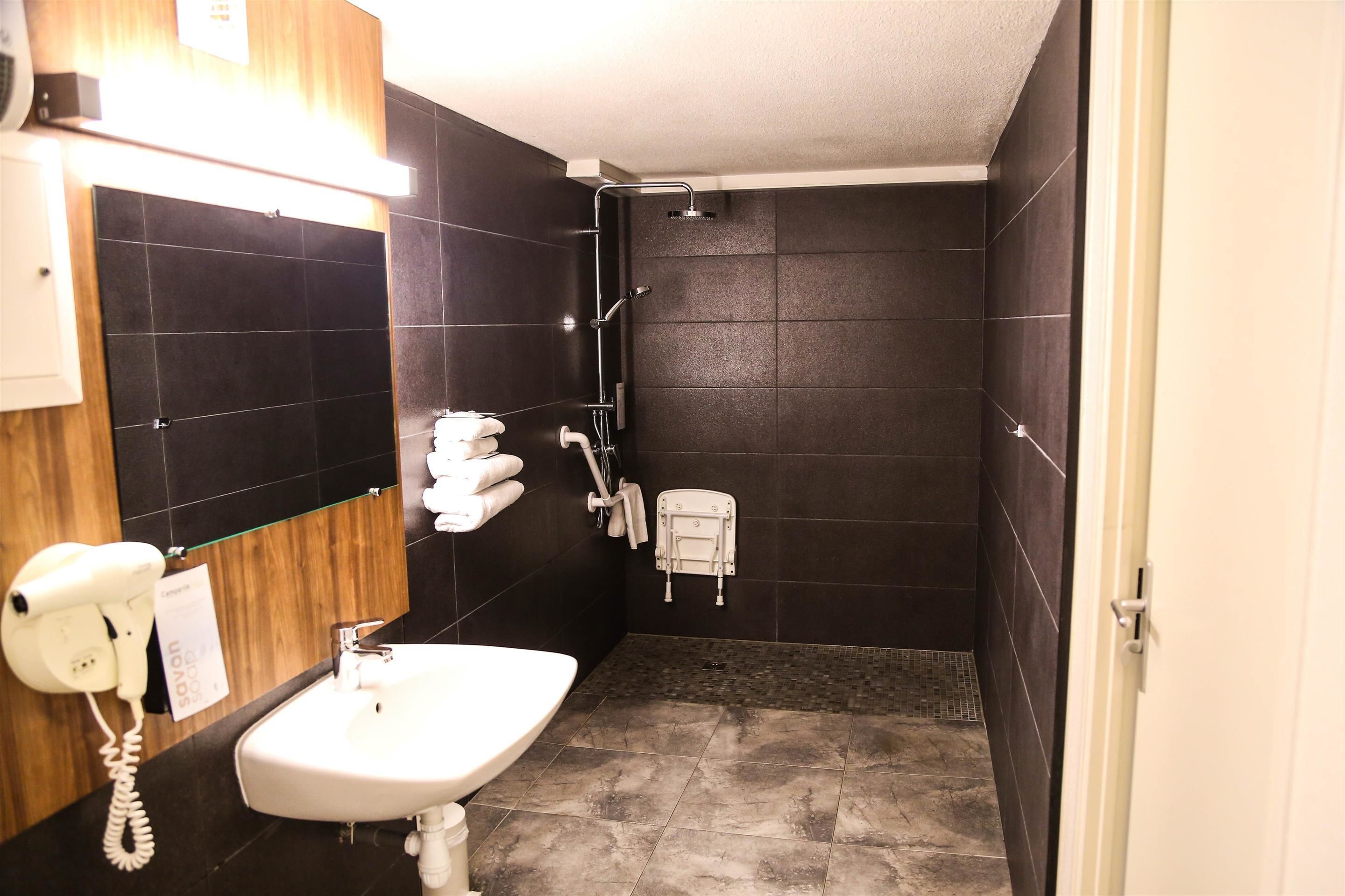 Une salle de bain équipée d’un lavabo, d’un miroir, d’un sèche-cheveux et d’une douche.